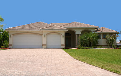 front view a generic florida home sits on a small grass covered hill with garage, palm trees and a clear blue sky, looking up the driveway.